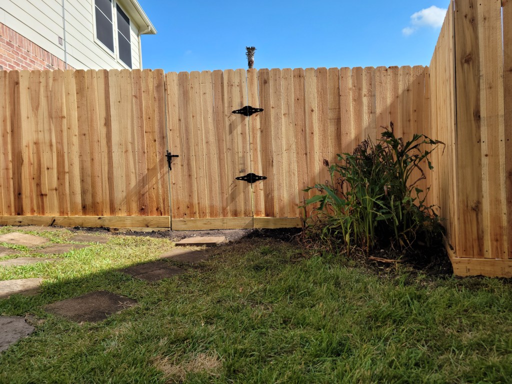 A newly installed wooden privacy fence with a double gate in a residential backyard, featuring a well-maintained lawn and decorative stone path.